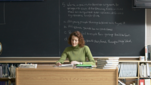 Substitute teacher reads at desk by chalkboard